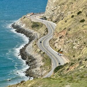 A road going down the side of a cliff next to water.