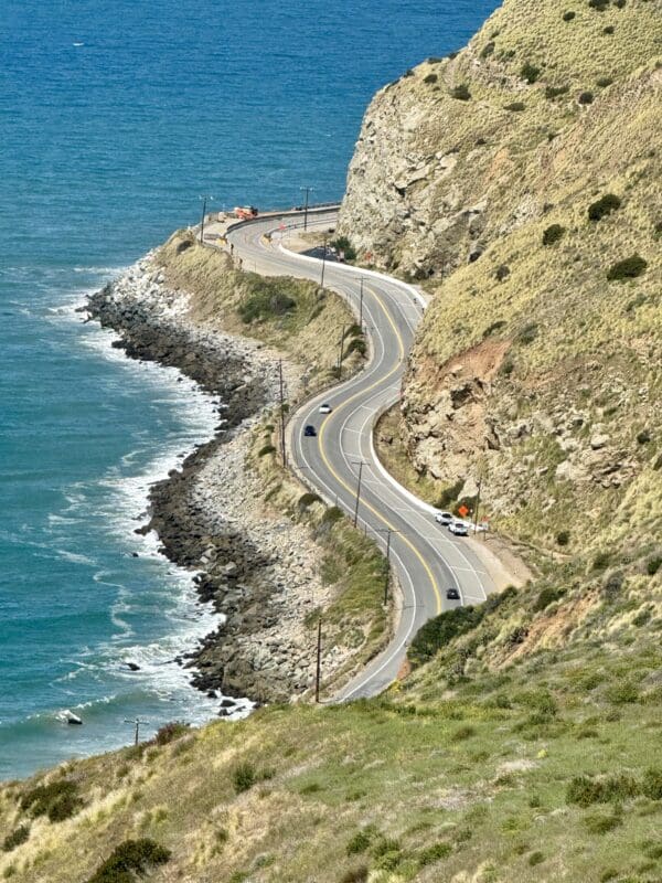 A road going down the side of a cliff next to water.