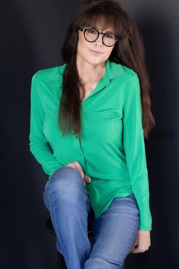 A woman in green shirt and jeans sitting on ground.